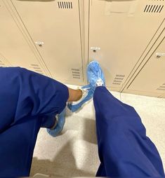 a person in blue scrubs is standing near lockers with their feet on the floor