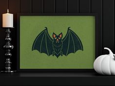 a framed photo of a bat on a shelf next to a white pumpkin and candle