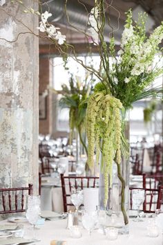 an arrangement of flowers and greenery in a tall glass vase on top of a table