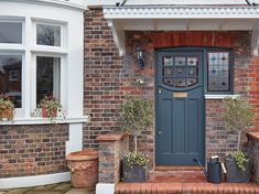 a blue front door to a brick building with potted plants on the steps and windows