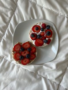 two small sandwiches with fruit on them sit on a white plate atop a bed sheet