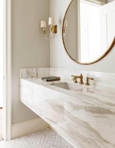 a white bathroom with marble counter tops and gold faucet lights on the wall