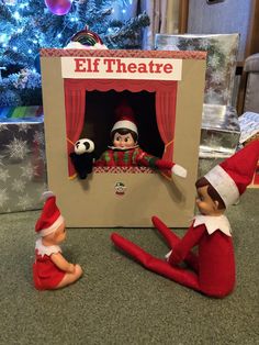 two elfs are sitting in front of a christmas tree and an elf theatre sign