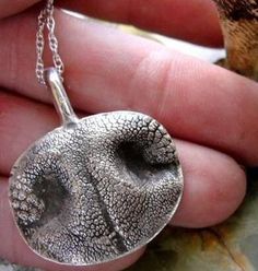 a hand holding a silver pendant with an animal's face on it