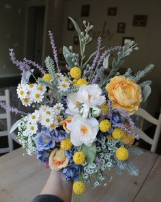 a person holding a bouquet of flowers on top of a wooden table