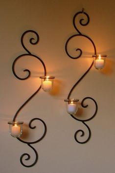 three candle holders are hanging on the wall with swirly designs and lights in them