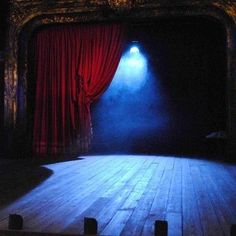 an empty stage with a red curtain and light coming from the top, in front of a wooden floor