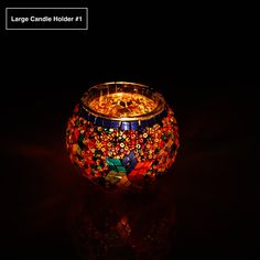 a colorful candle holder sitting on top of a black table next to a dark background