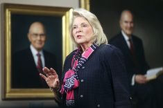 an older woman standing in front of two framed pictures and holding her hands out to the side