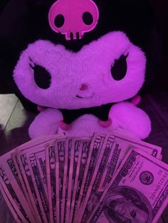 a hello kitty stuffed animal sitting on top of a pile of money next to a fan of hundred dollar bills