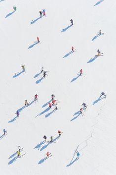 an aerial view of people skiing down a snow covered slope, with shadows on the ground