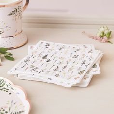 three napkins with flowers on them sitting next to a cup and saucer