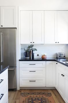 a kitchen with white cabinets and black counter tops, an area rug on the floor