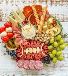 a football shaped platter filled with meats, cheeses, and fruit on top of a white wooden table