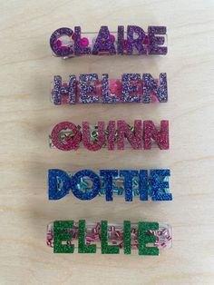 three different colored glitter name stickers sitting on top of a wooden table