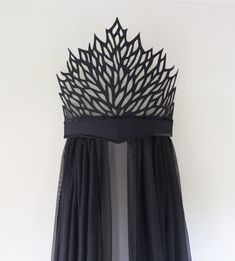 a black dress hanging on a wall with sheer fabric over it and an intricate cut out design