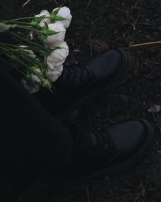 a person wearing black shoes with white flowers in their lap and one foot on the ground