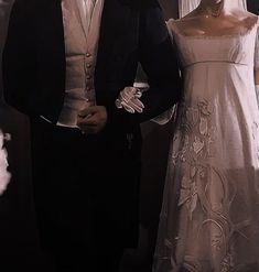 a man and woman standing next to each other in front of a wedding dress on display