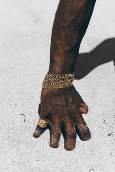 a man's hand with gold chains on it and his hands in the sand