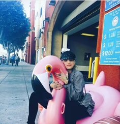 a woman sitting on an inflatable pink flamingo next to a bank atm