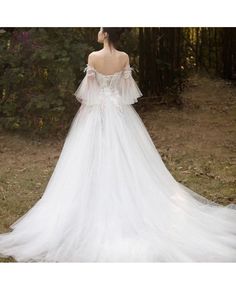 a woman in a white wedding dress standing on the grass with her back to the camera