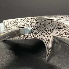 an old silver knife with ornate designs on it's blade and handle, resting on a black surface