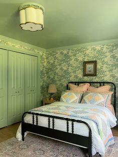 a bed sitting in a bedroom next to a green wallpapered wall and a lamp