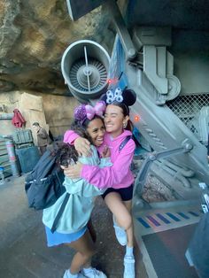 two young women hugging each other in front of mickey mouse