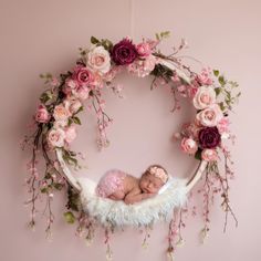 a baby is sleeping in a floral wreath with pink flowers on the wall behind it