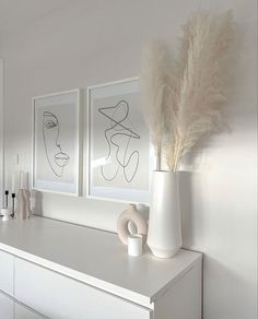 two white vases sitting on top of a white dresser next to paintings and candles