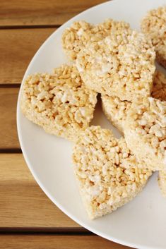 several pieces of rice krispy treats on a white plate next to a wooden table