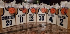 basketball themed gift bags are lined up on a table in front of a wall with the names and numbers of each team