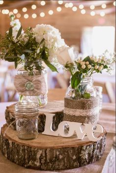 two mason jars filled with white flowers on top of a wooden slice that says love