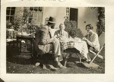 an old black and white photo of three people sitting at a table outside in the grass