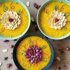 three bowls filled with food sitting on top of a wooden table next to flowers and petals