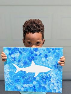 a young boy holding up a painting with a shark on it