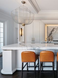 two stools sit at the center of a kitchen island with marble countertops and white cabinets