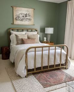 a bedroom with green walls and white bedding, rugs on the floor and a painting above the bed