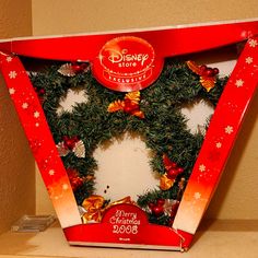 a christmas wreath in a red box with snowflakes on it and decorations around the edges