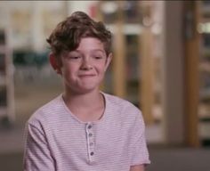 a young boy is smiling and looking at the camera while wearing a pink striped shirt