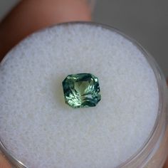 a green diamond sitting on top of a glass container in someone's left hand