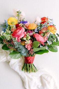 a bunch of flowers that are sitting on a white table cloth with green leaves and red ribbon