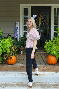 a woman standing on steps in front of a house with pumpkins and plants behind her