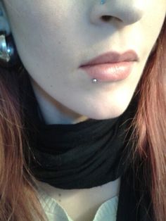 a close up of a woman with red hair and piercings on her nose wearing a black scarf