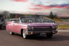 an old pink car parked on the side of the road with a trailer behind it