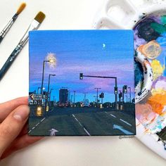 a person holding up a piece of art with paint and brushes on the table next to it