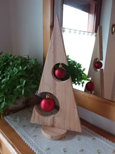 a wooden christmas tree with red ornaments on it's stand next to a potted plant