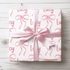 a wrapped gift box with pink ribbon and bow on white wooden background, top view