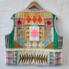 a colorful patchwork vest hanging on a white brick wall with a wooden hanger