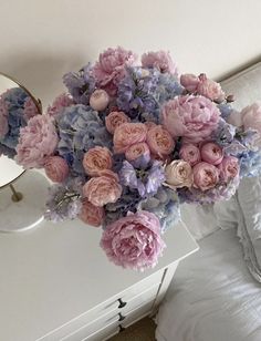 a vase filled with pink and blue flowers sitting on top of a bed next to a mirror